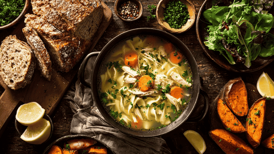 Low-sodium chicken noodle soup with sides like whole-grain bread, salad, roasted veggies, and sweet potato wedges.